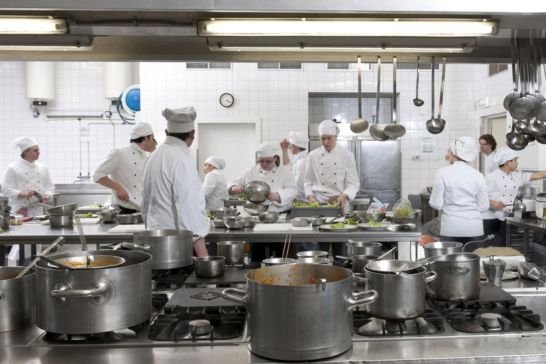 Chefs trabajando en cocina profesional equipada con hornos, freidoras y cocinas industriales, ideal para servicio técnico gastronómico en Buenos Aires